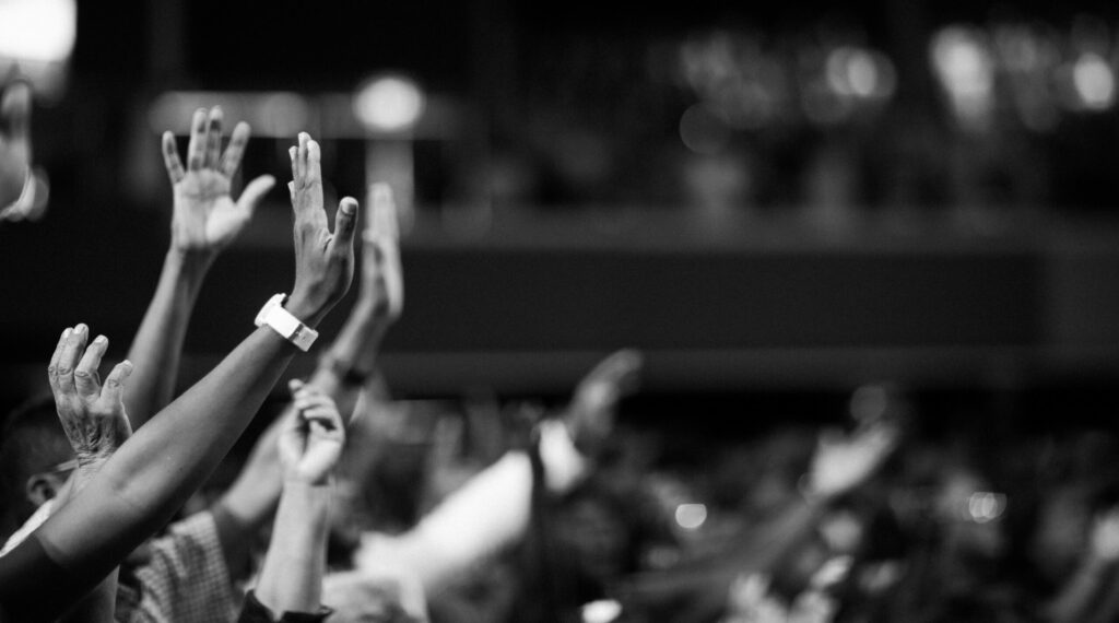 black & white image showing arms of a congregation raised in praise to Jesus